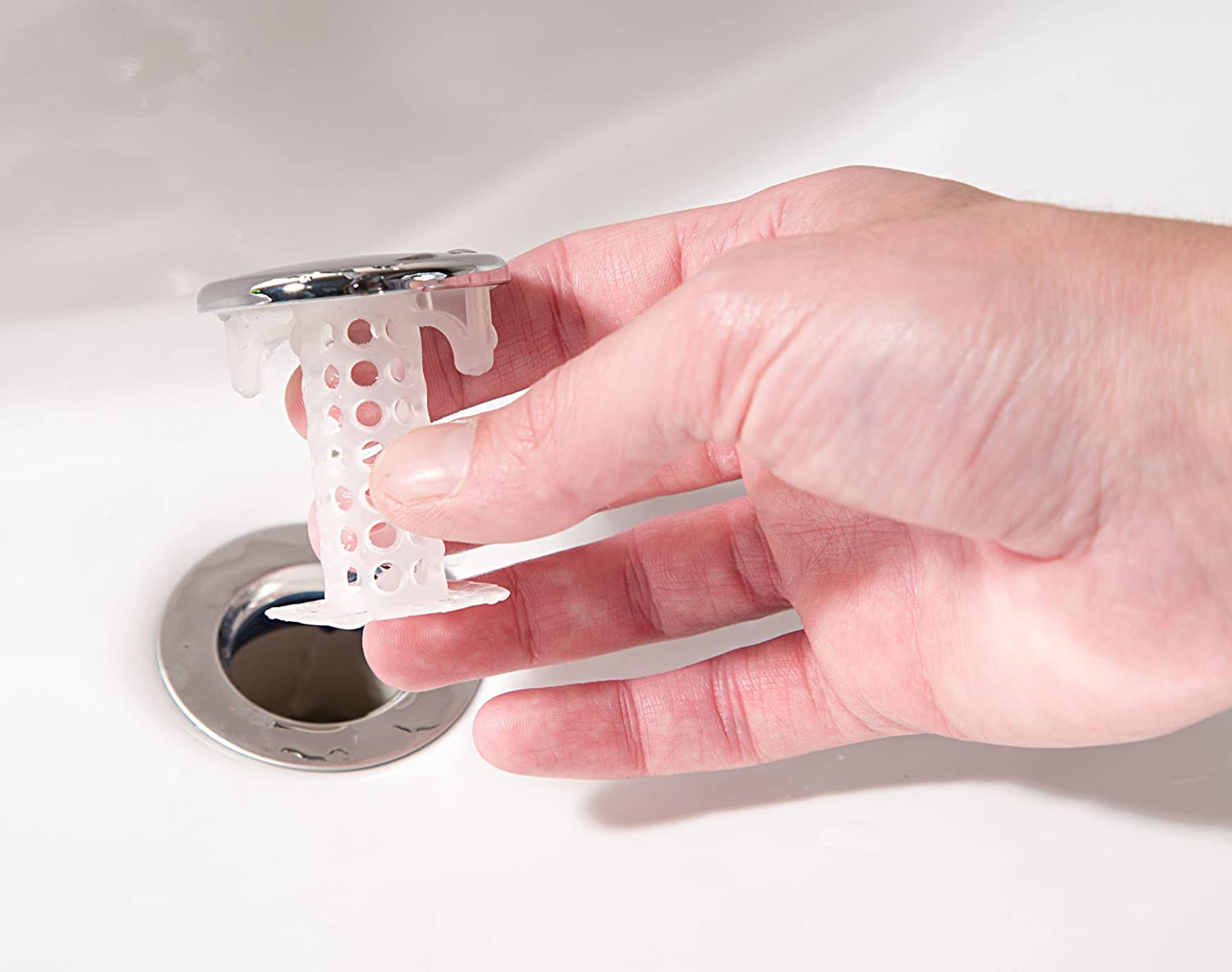 A human hand holds the chrome SinkShroom in preparation to install it in an empty drain